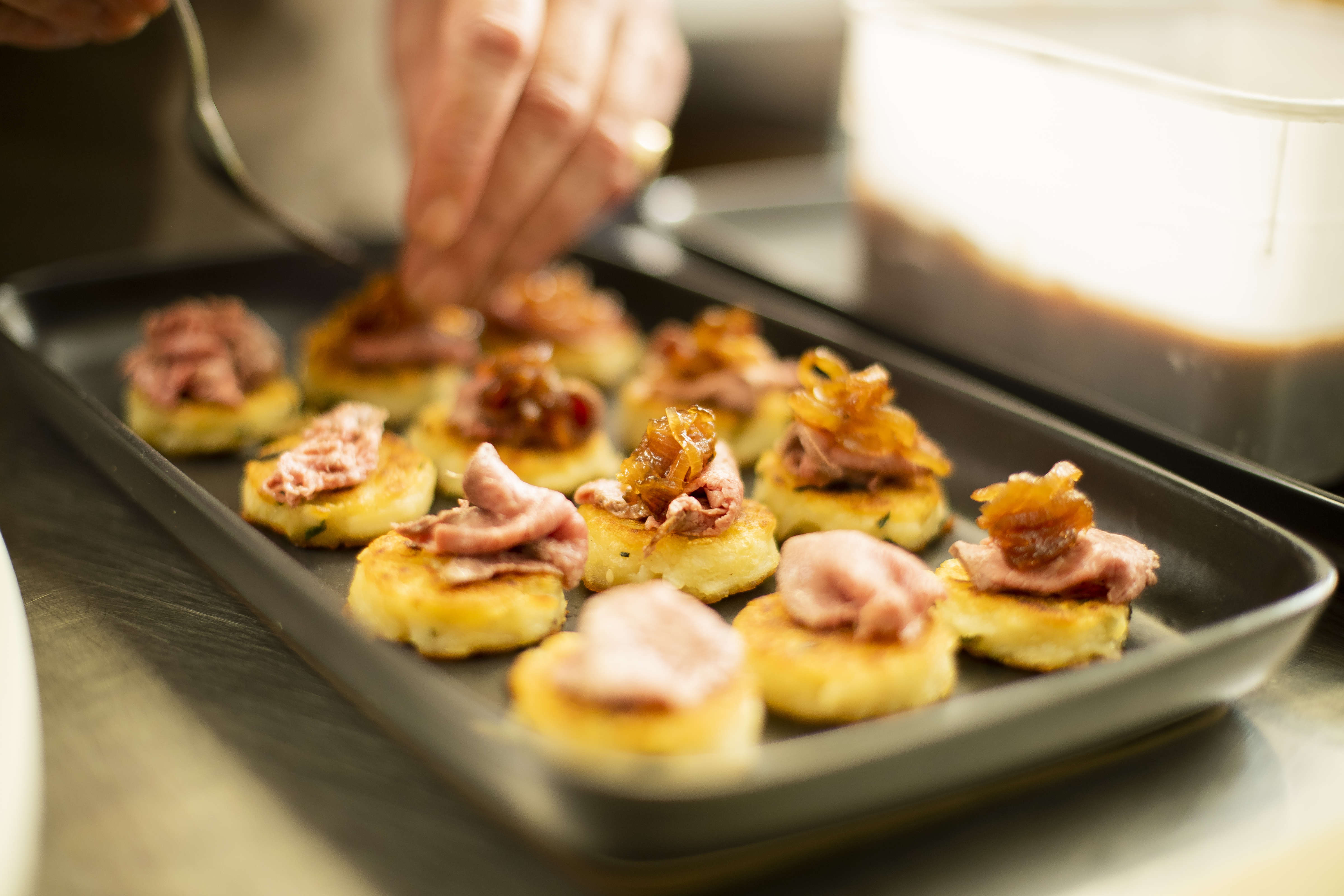 Close up of chef garnishing a platter of hashbrowns with rare roast been and caramelised onion. Photo: Richard Jupe.